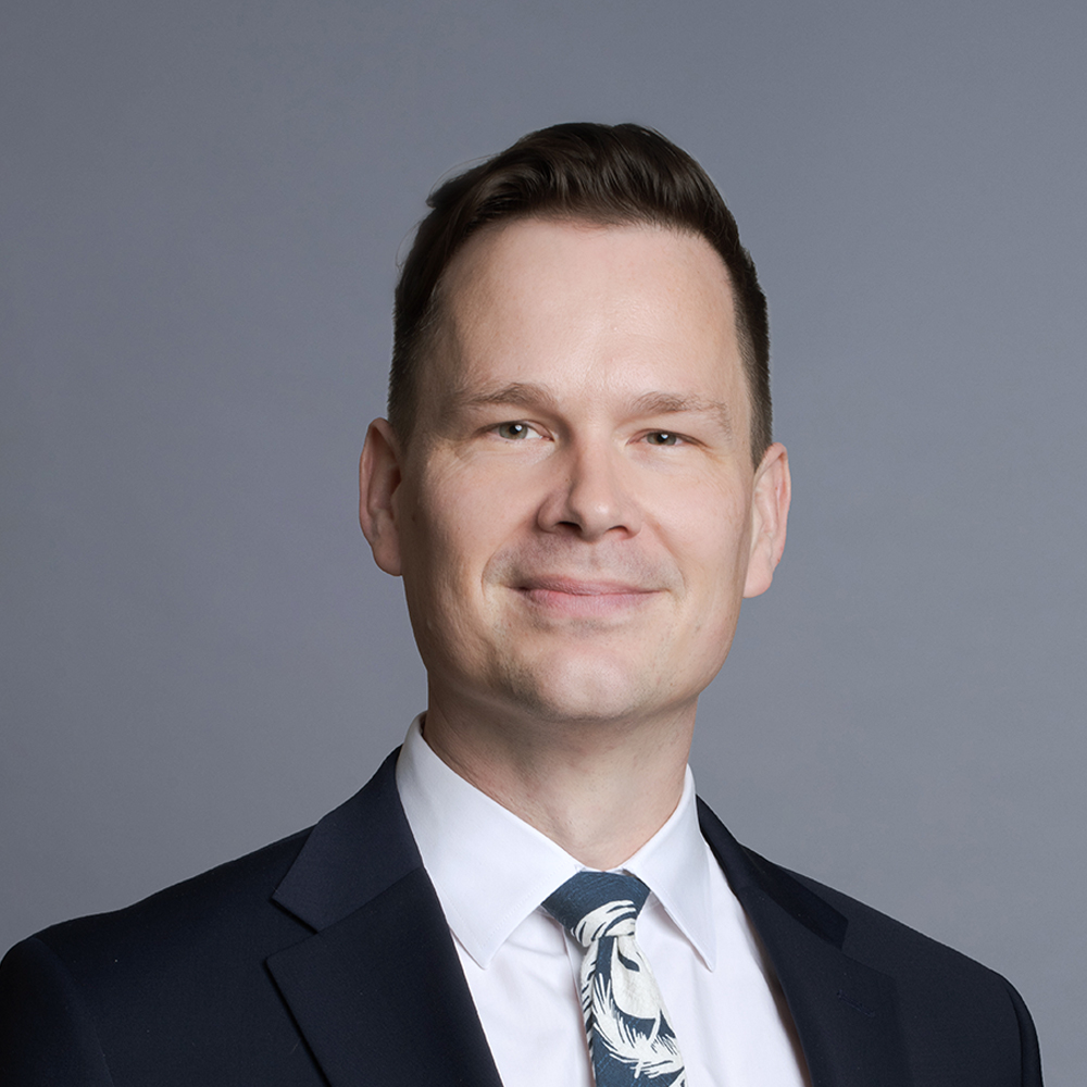 White man in a suit and tie posing against a gray background.