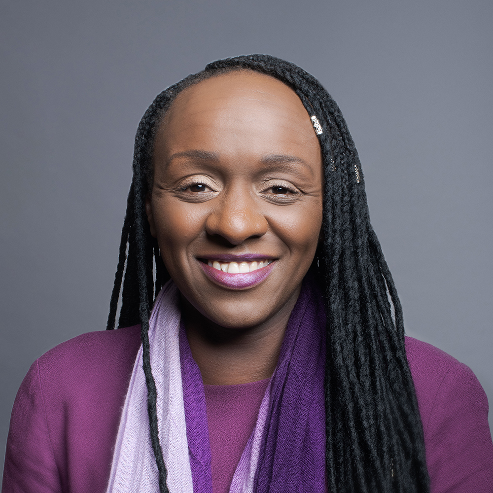 Black woman in a purple shirt posing against a gray background.