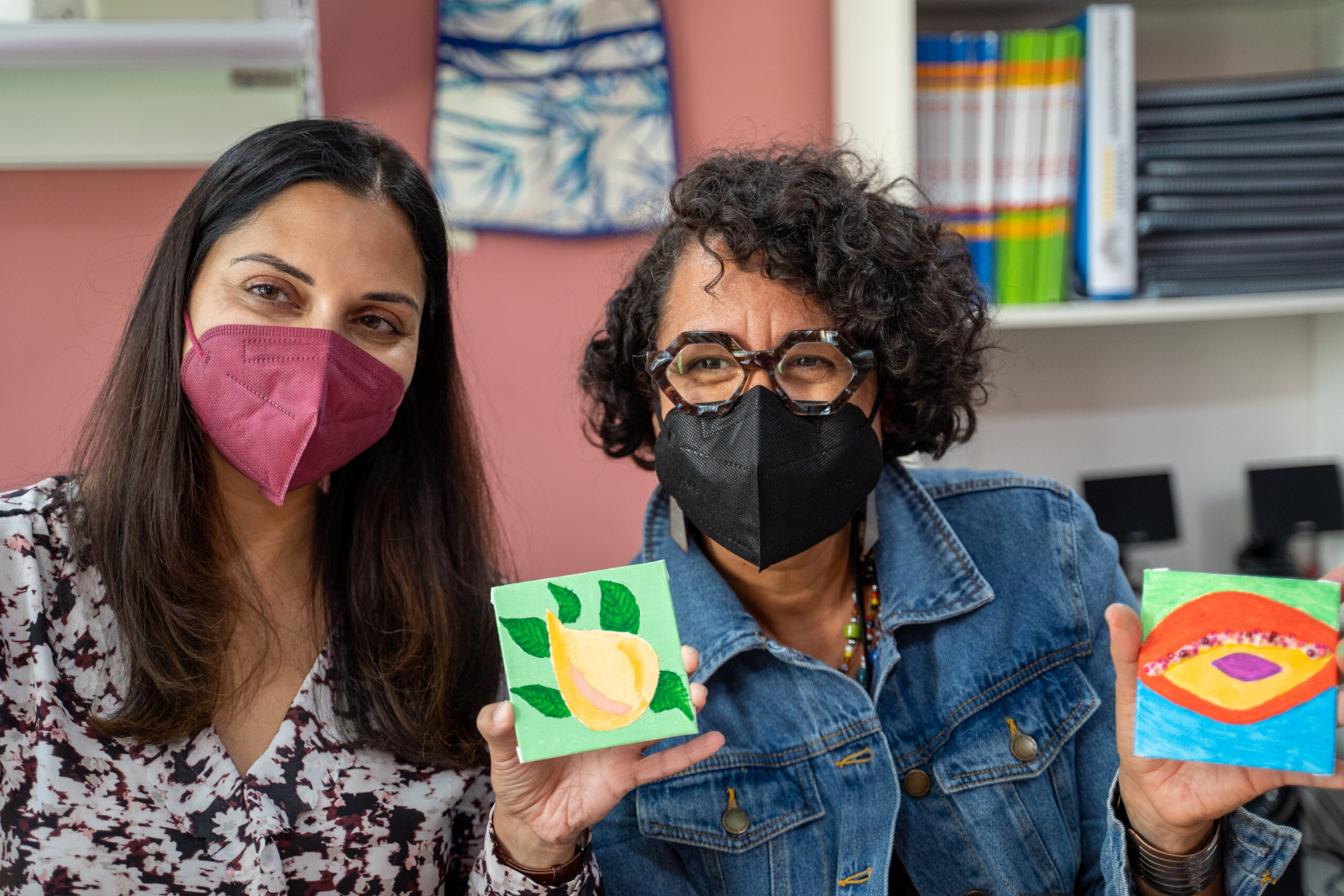 two women wearing masks holding up pieces of art.