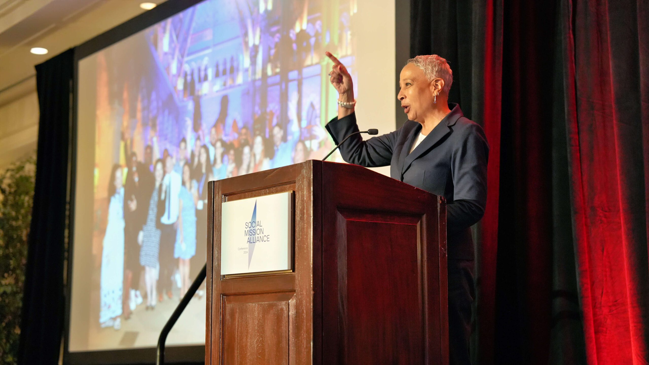 Brigit Carter standing at a podium and pointing to the crowd at the Social Mission Alliance Conference