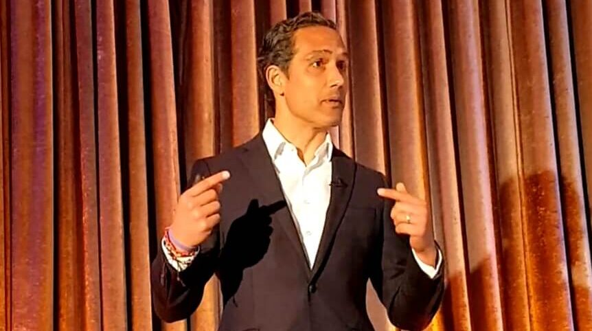 Man speaking in front of a backdrop.