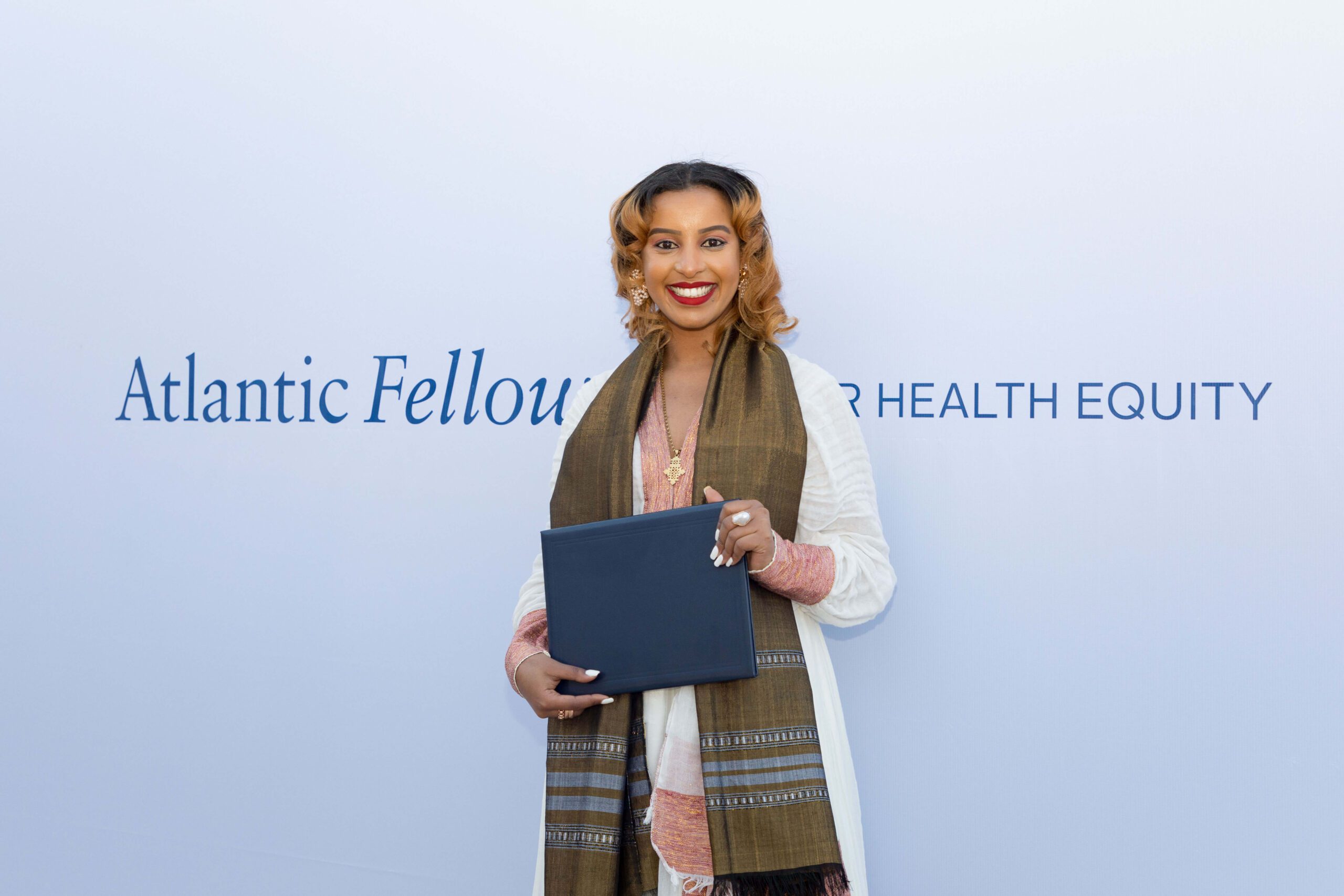 Woman holding a certificate in front of a wall with AFHE logo.