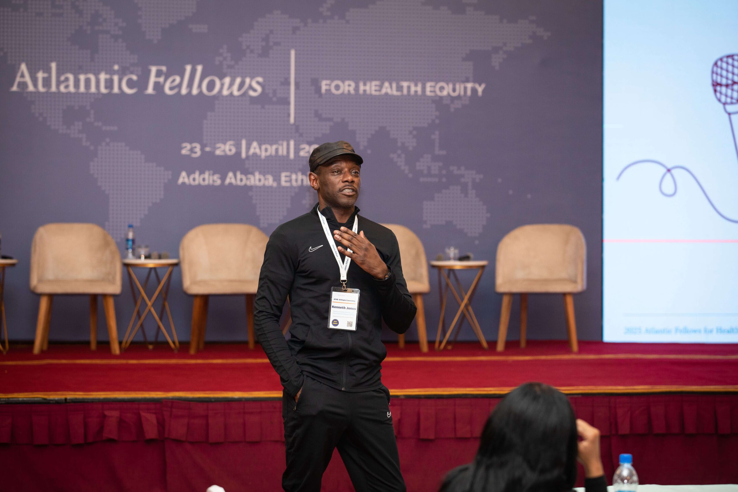 Man stands in front of a stage, talking.