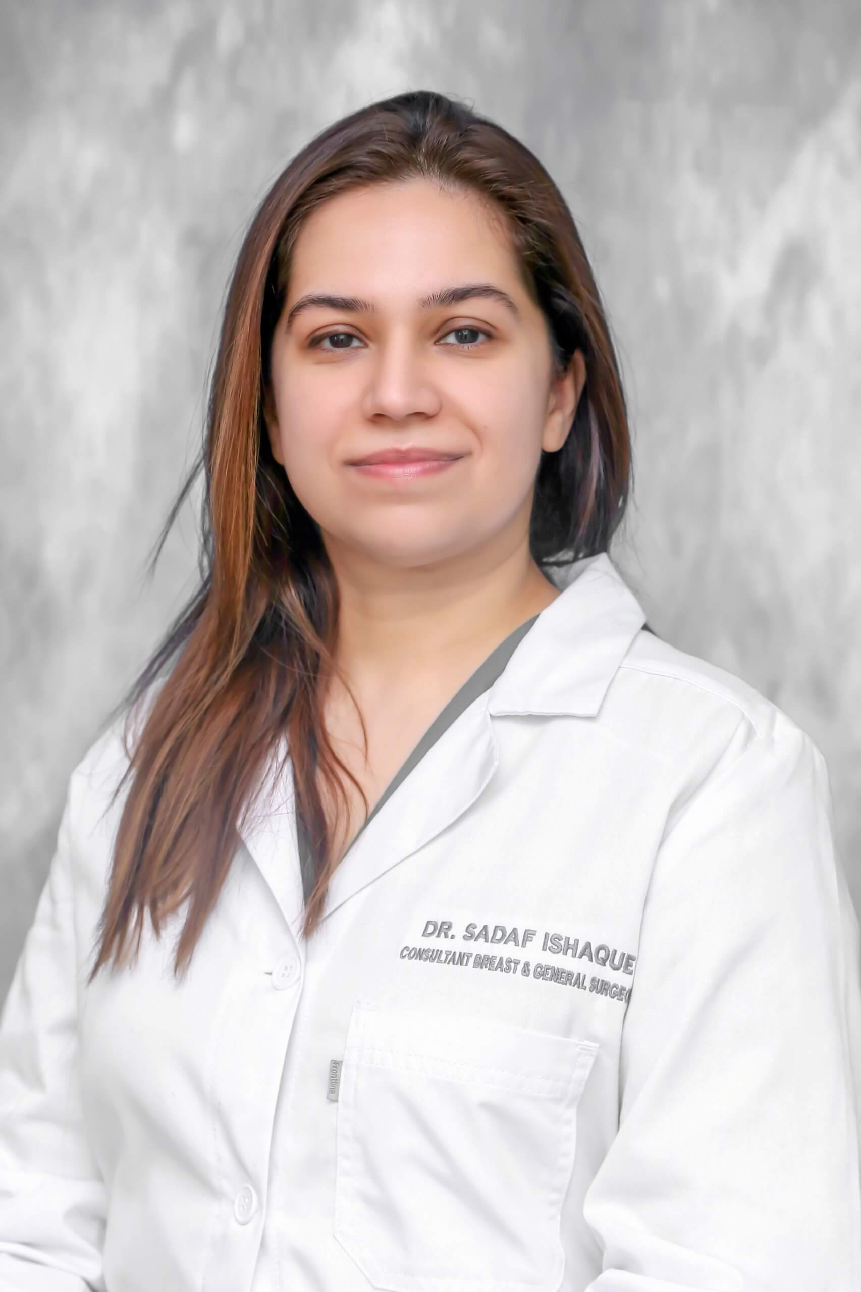 Woman in a white lab coat posing for a headshot on a light gray background.