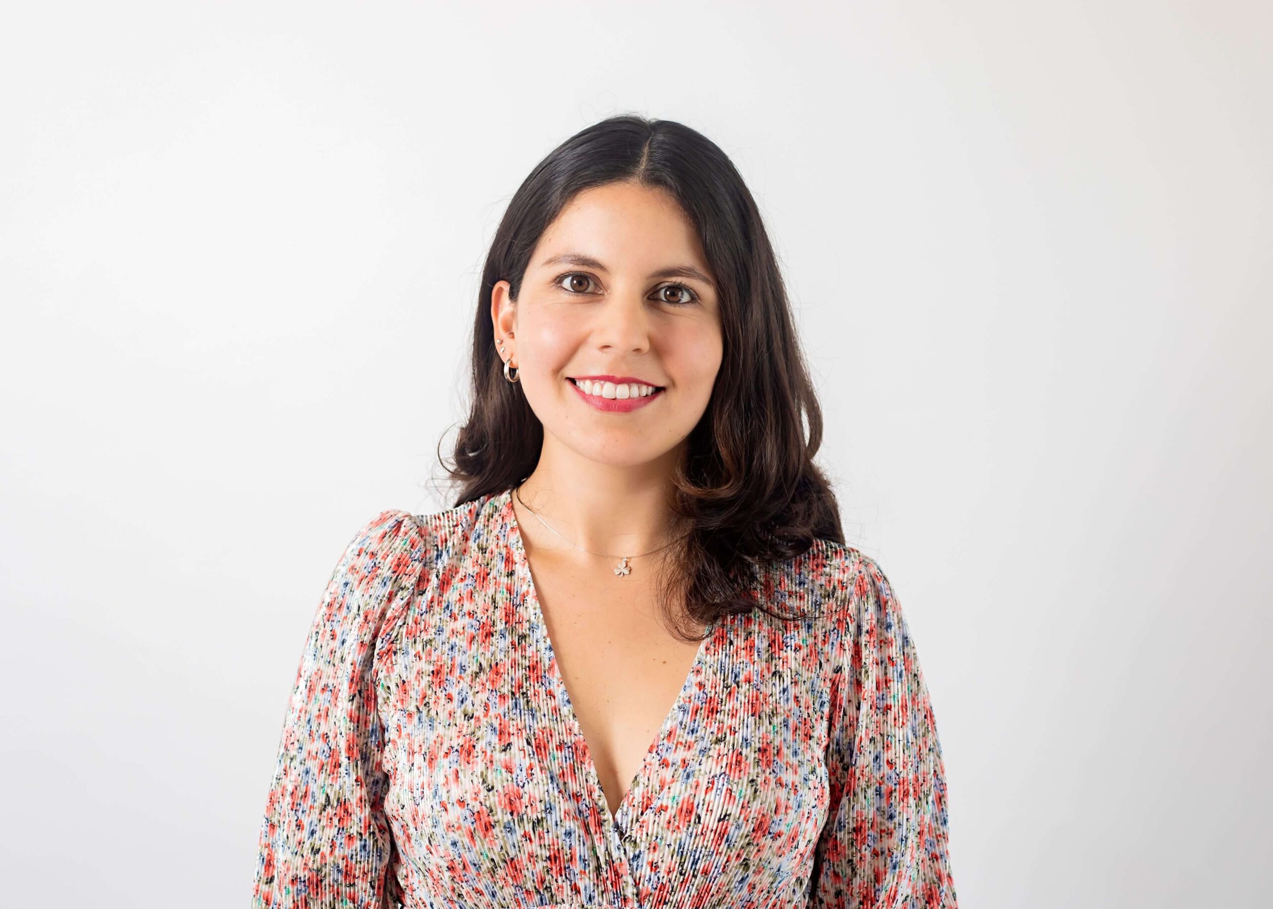 Woman in a flowery dress posing for a headshot in front of a light gray background.
