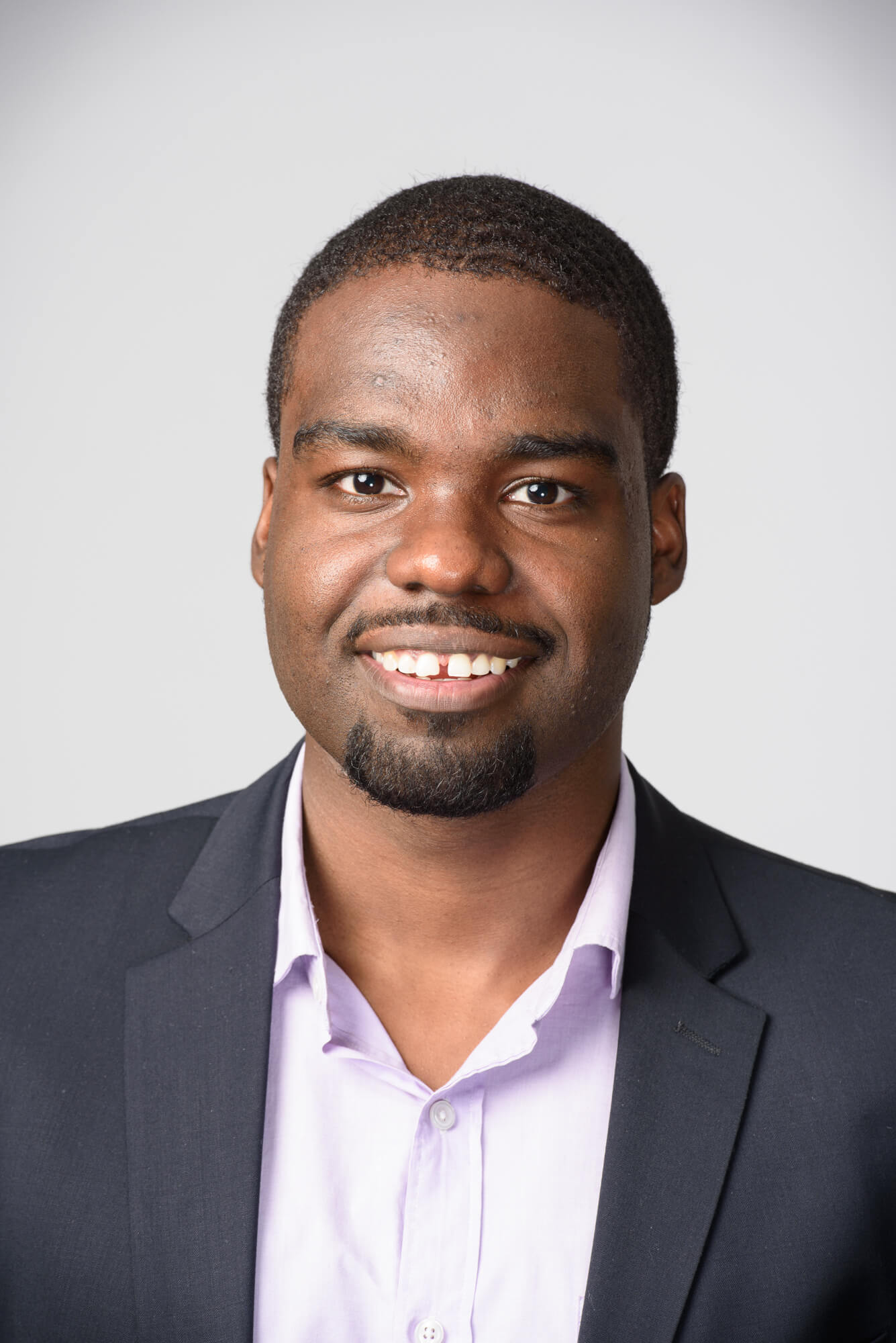 Black man in a suit jacket against a light background posing for a headshot.