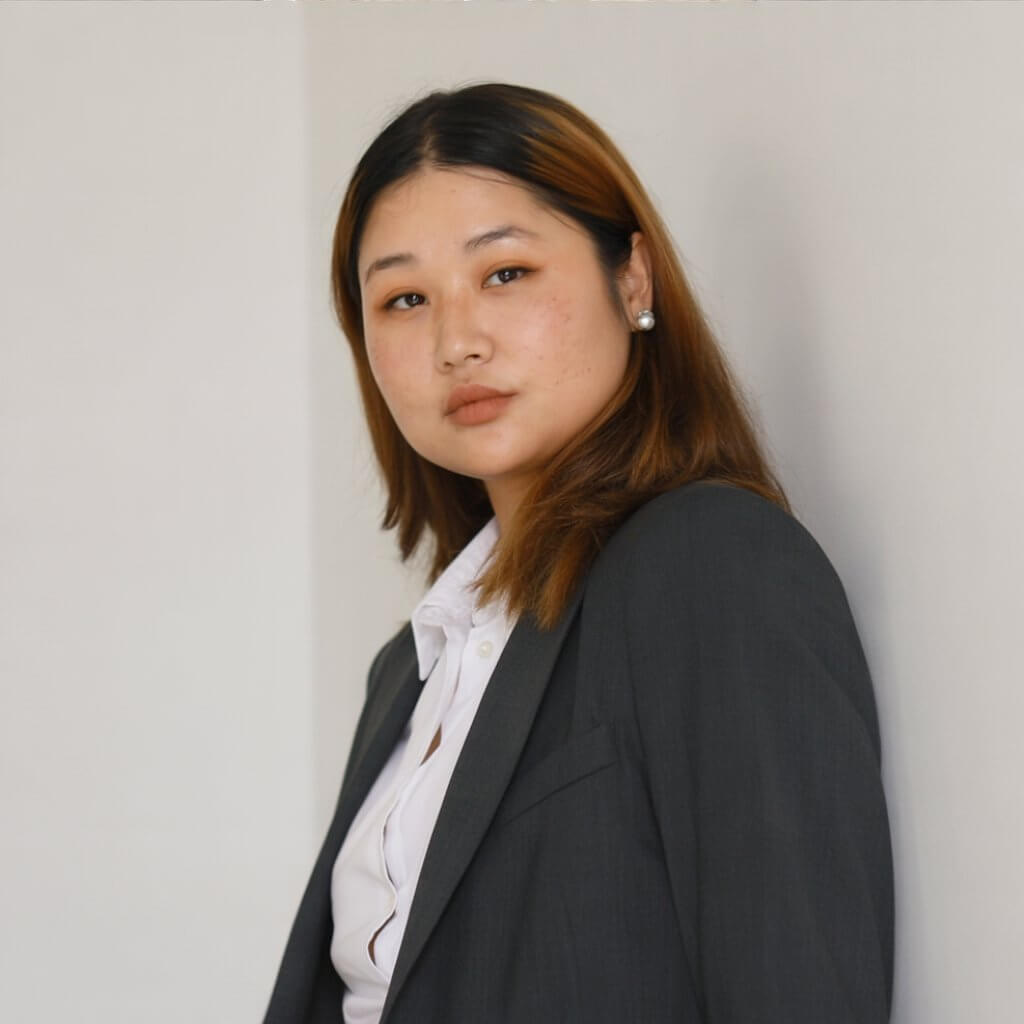 Woman in a blazer leaning against a wall posing for a headshot