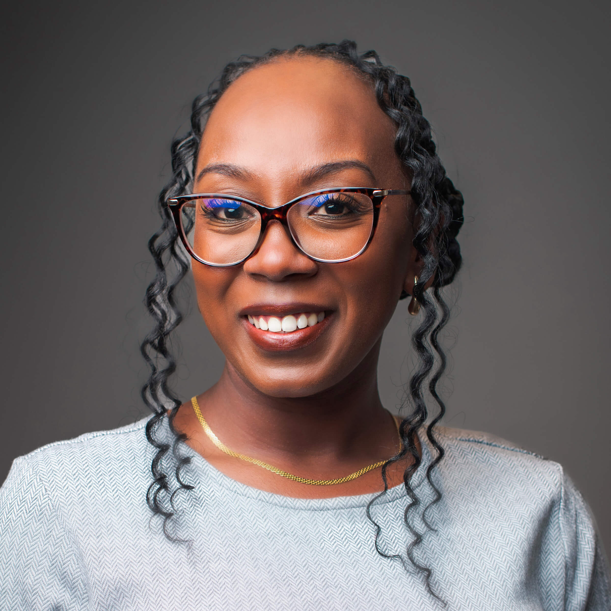 Black woman posing for a headshot against a gray background.