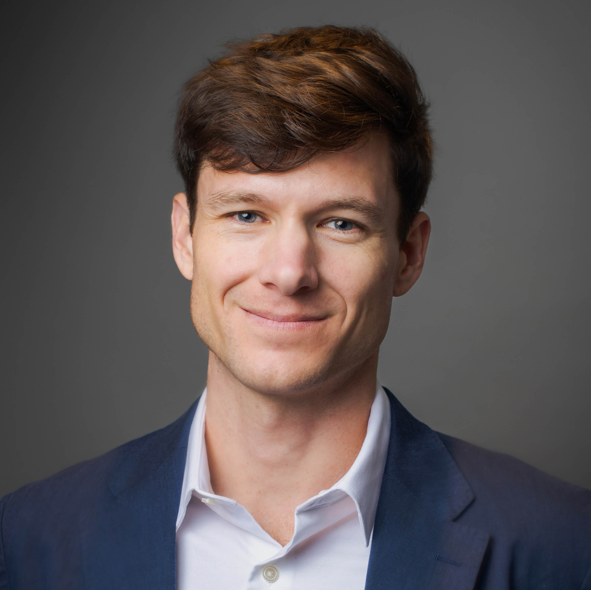White man posing for a headshot against a gray background.