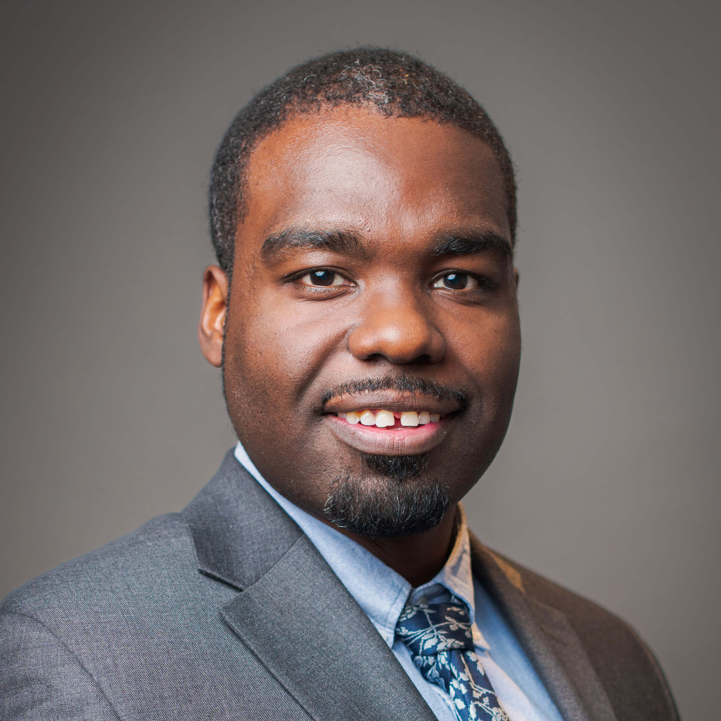 Black man posing for a headshot against a gray background.