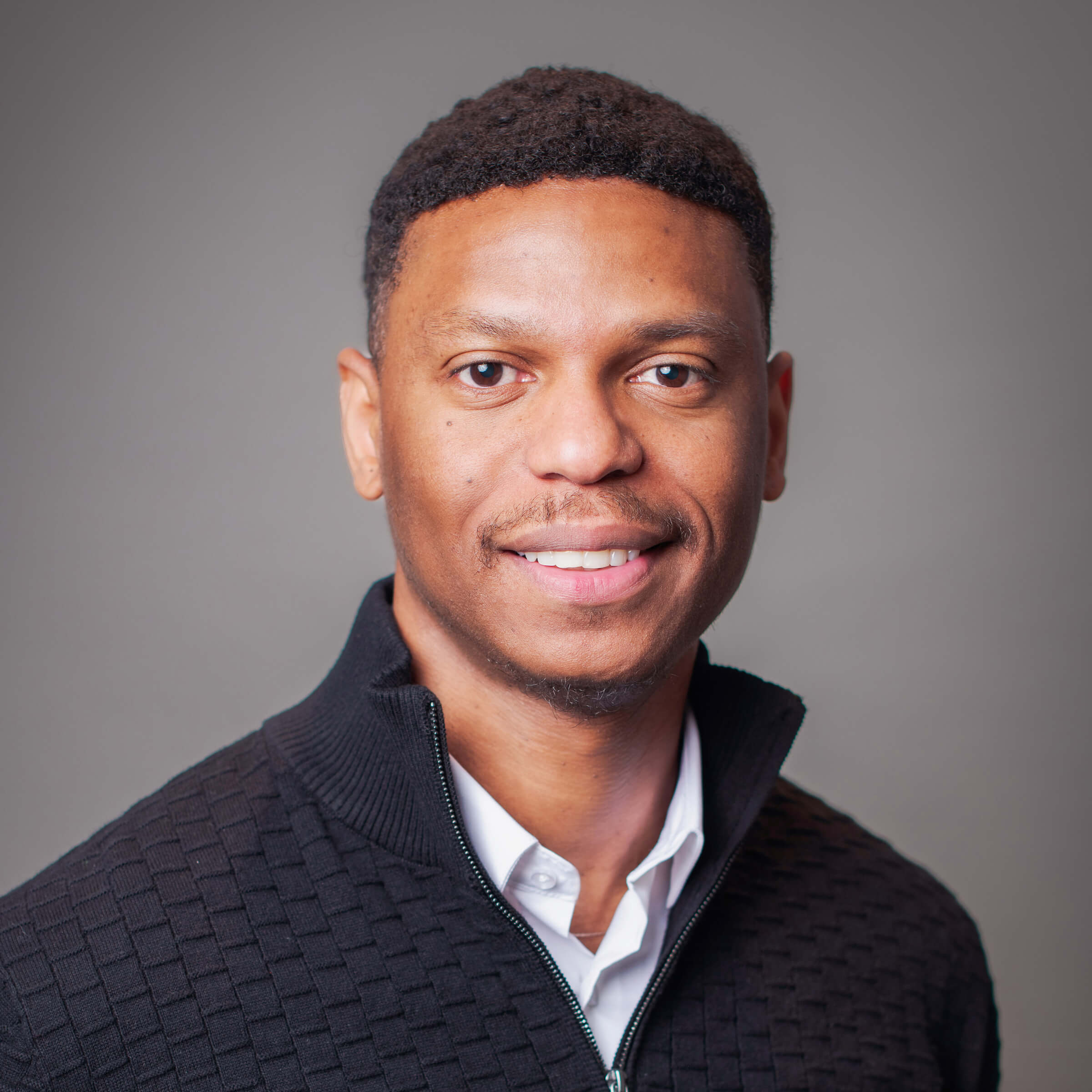 Black man posing against a gray background.
