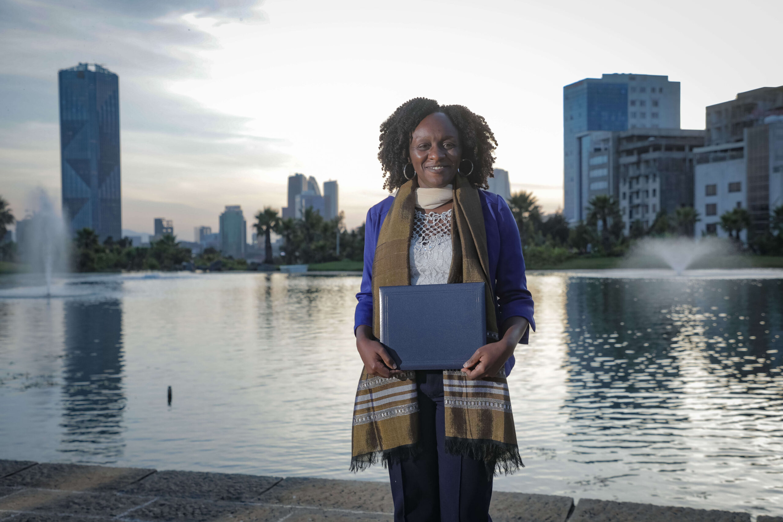 Black woman holding a booklet standing in front of a body of water