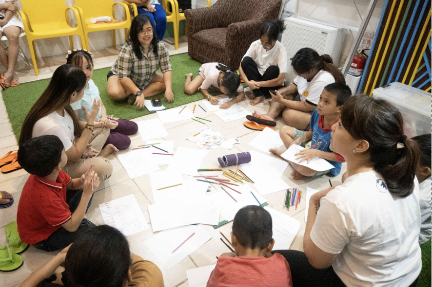 group of people sitting in a circle, mostly kids with some adults.