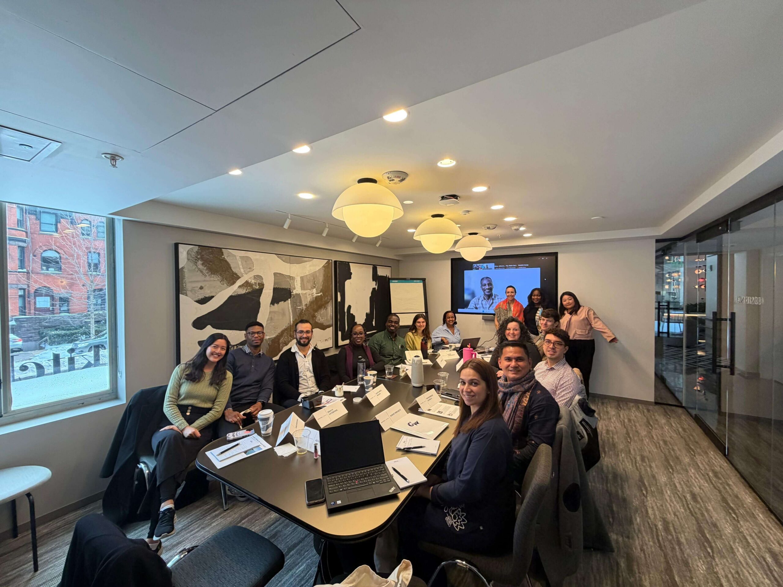 Members of a conference group pose around a long boardroom table inside a modern meeting room with abstract artwork on the wall.