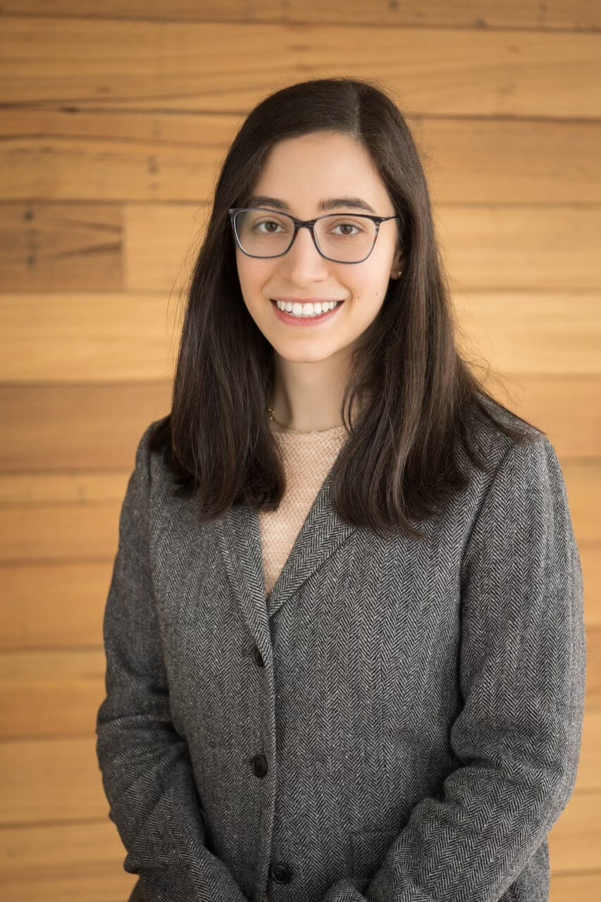 Woman posing for a headshot in front of wood paneling.