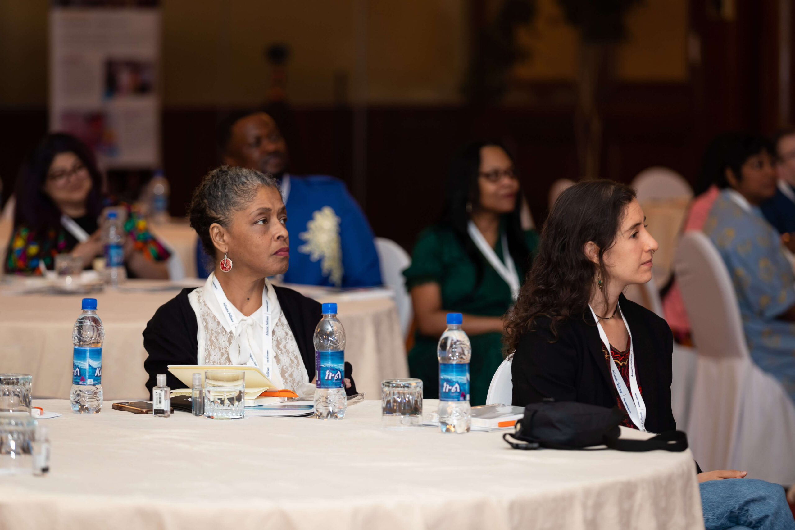 Conference attendees seated at a round table listening to a speaker.