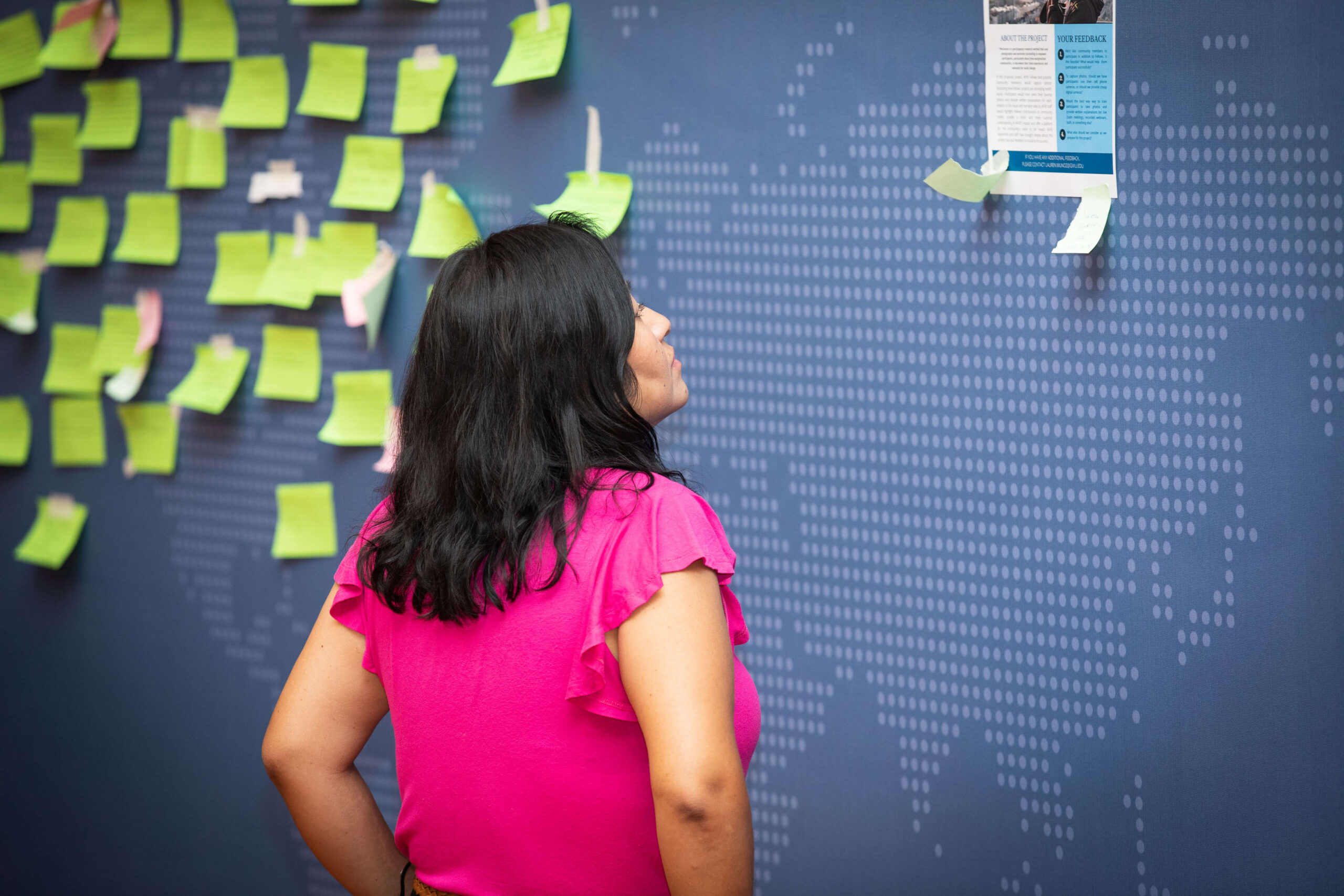 A woman looking at a wall map covered with sticky notes.